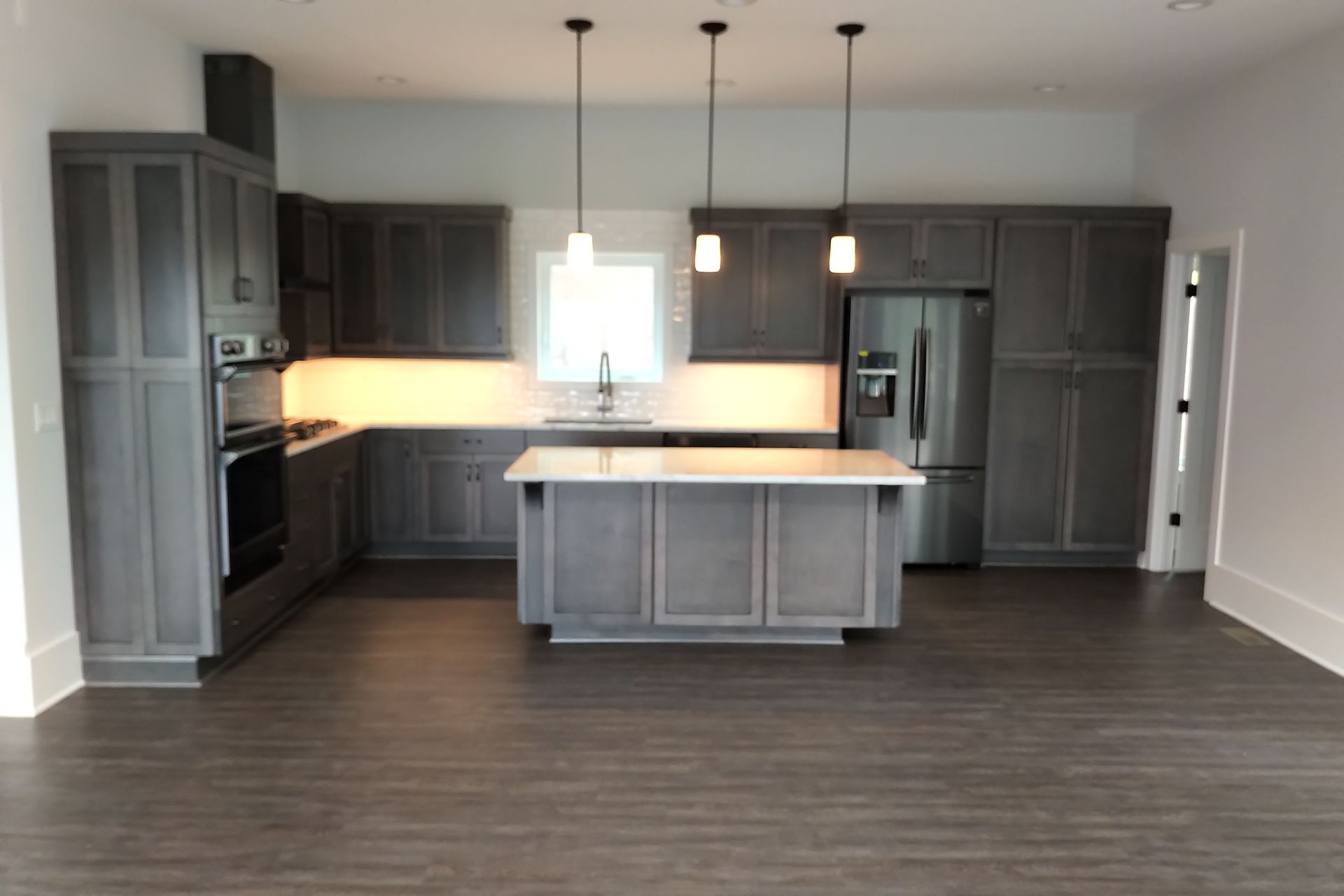 Gray kitchen with dark wood floors, island, stainless steel appliances, and pendant lights.