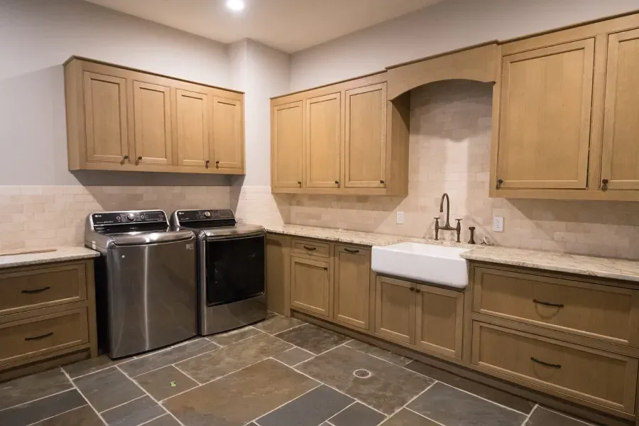 Laundry room with cabinets, sink, and washer/dryer on stone tile floor.