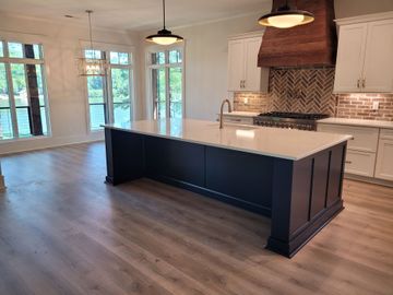 Kitchen with navy island, white cabinets, wooden range hood, and light wood floors.