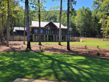 Modern house nestled in a forest with a grassy lawn and a blue sky.