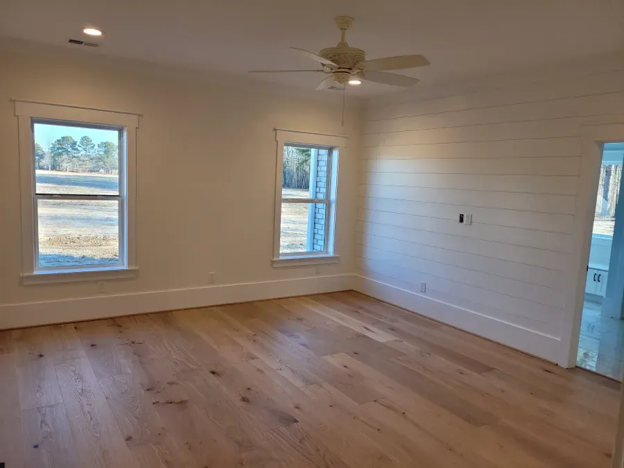 Empty room with hardwood floors, white walls, windows, and a ceiling fan.
