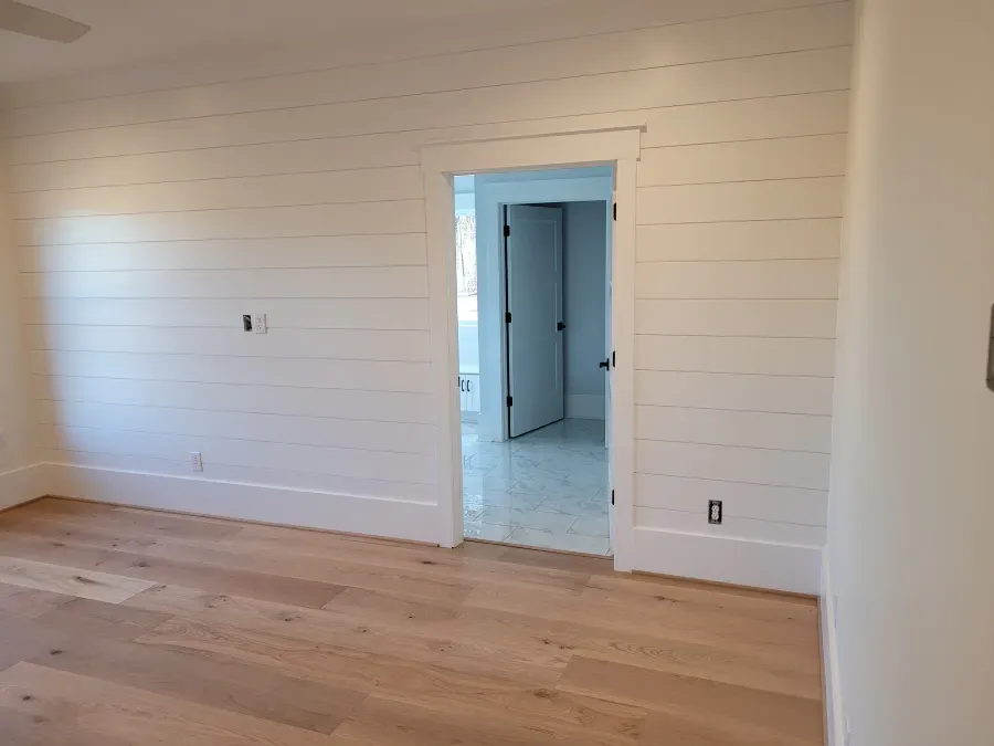 Bright room with white shiplap walls, light wood floor, and an open doorway to another room.