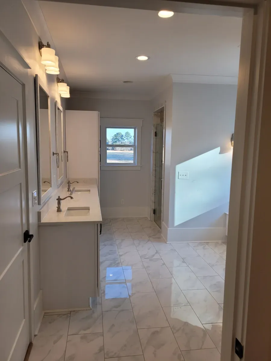 Bathroom with white marble floors, double vanity, and a window.