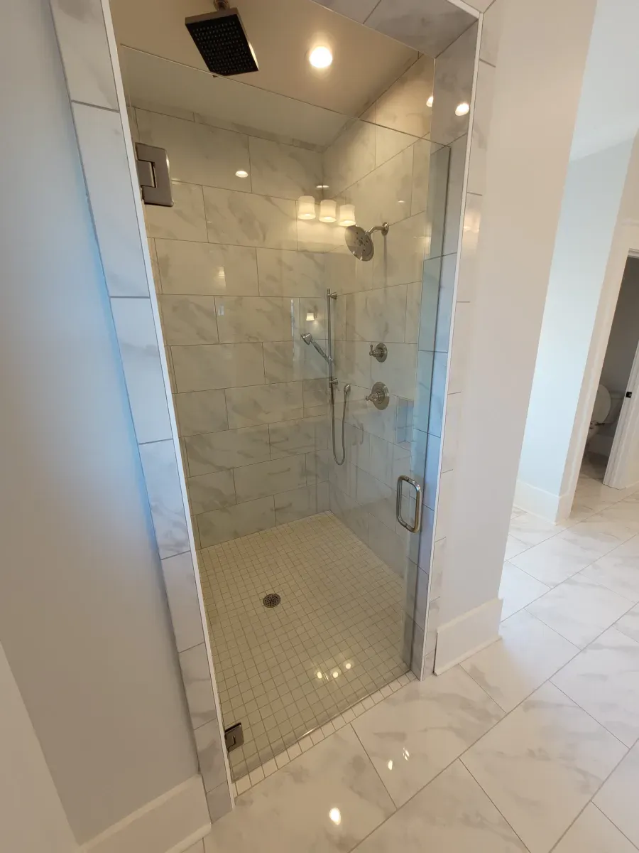 Glass shower with marble tile, a handheld showerhead, and a modern faucet, in a white bathroom.