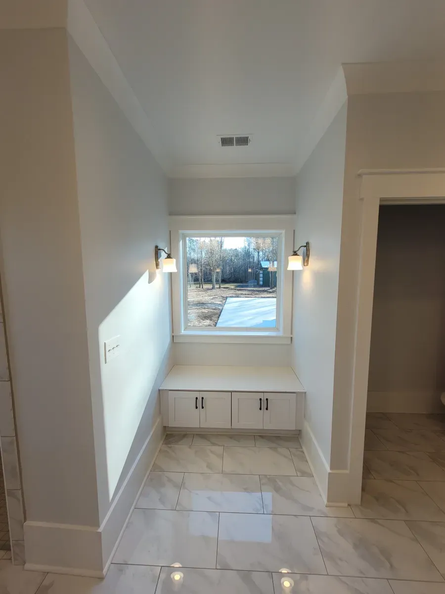 Hallway with window seat, white cabinets, sconces, and gray tile.