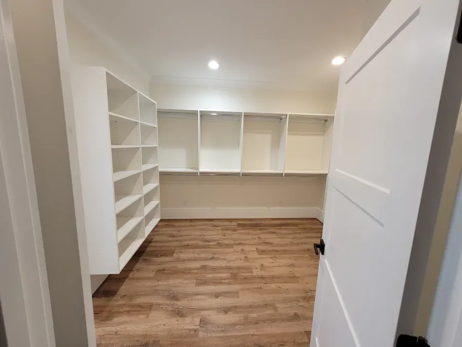 Empty white pantry with shelves, wood-look floor, and a partially open white door.