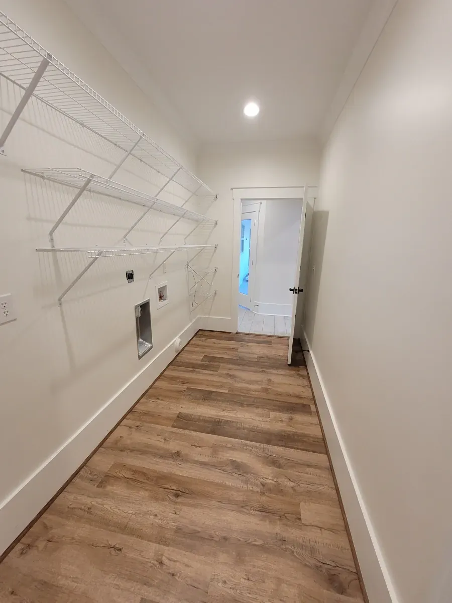 Laundry room with wood-look floor, white walls, wire shelves, and an open doorway.