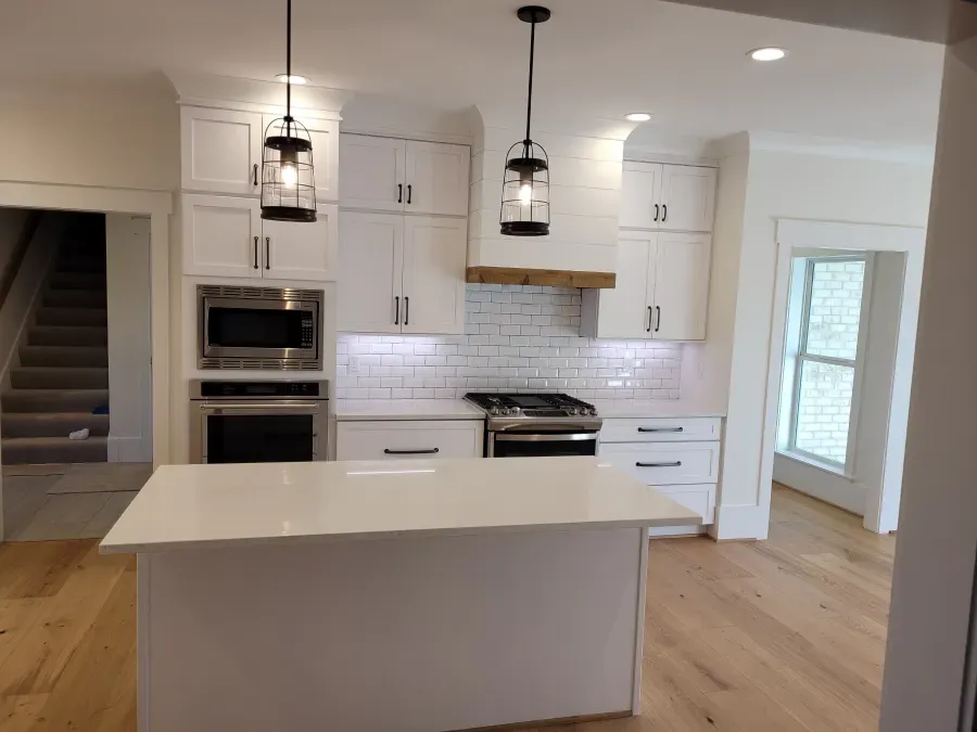 White kitchen with island, stainless steel appliances, and light wood floors. Two lantern lights hang above.