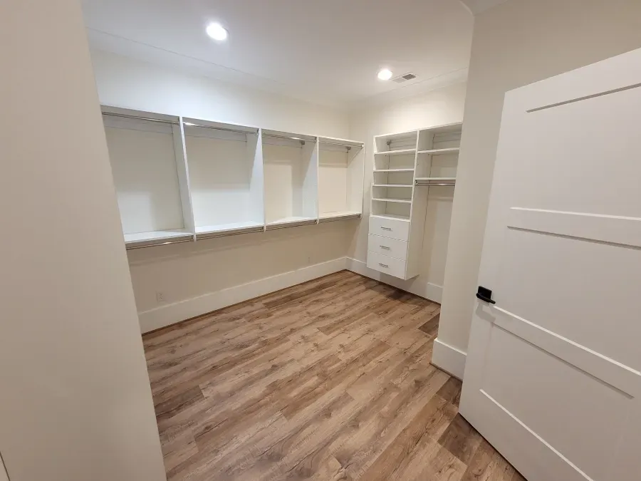 Walk-in closet with white shelving, a door, and wood-look flooring.