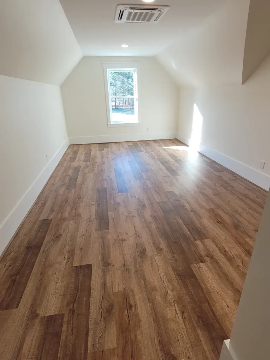 Attic room with wood-look floors, white walls, and a window.