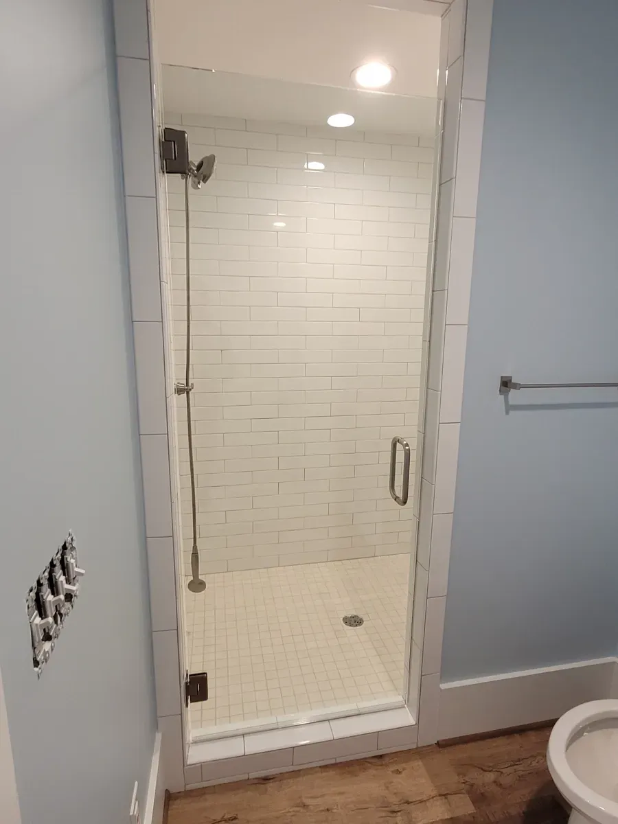 Glass shower with white tiled walls, light blue wall, and a silver towel rack.