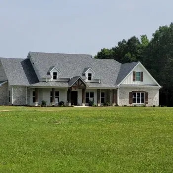 House with light brick exterior, gray roof, and green lawn. Brown shutters and trim.