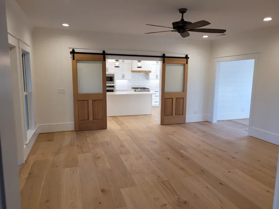 Wooden barn doors open to kitchen, hardwood floors, white walls, and a ceiling fan.