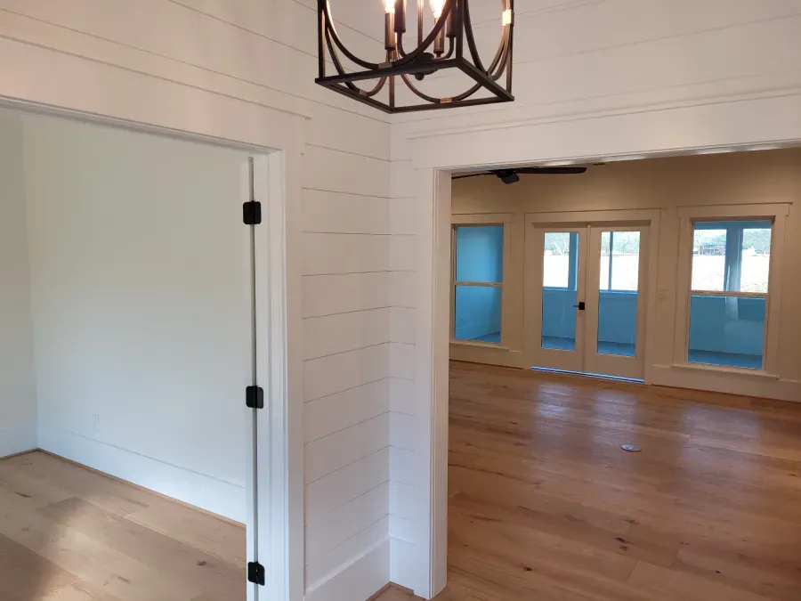 Interior with white shiplap walls, wood floor, and doorway leading to a room with French doors.