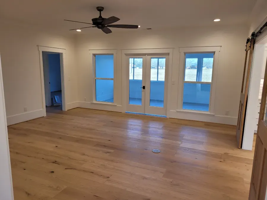 Empty room with wood floor, white walls, French doors, and a barn door.