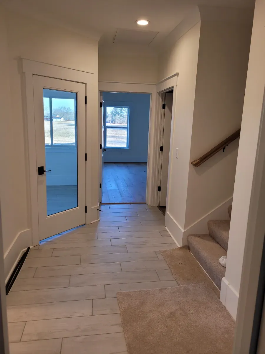 Hallway with tiled floor, stairs, doors to rooms, and natural light.
