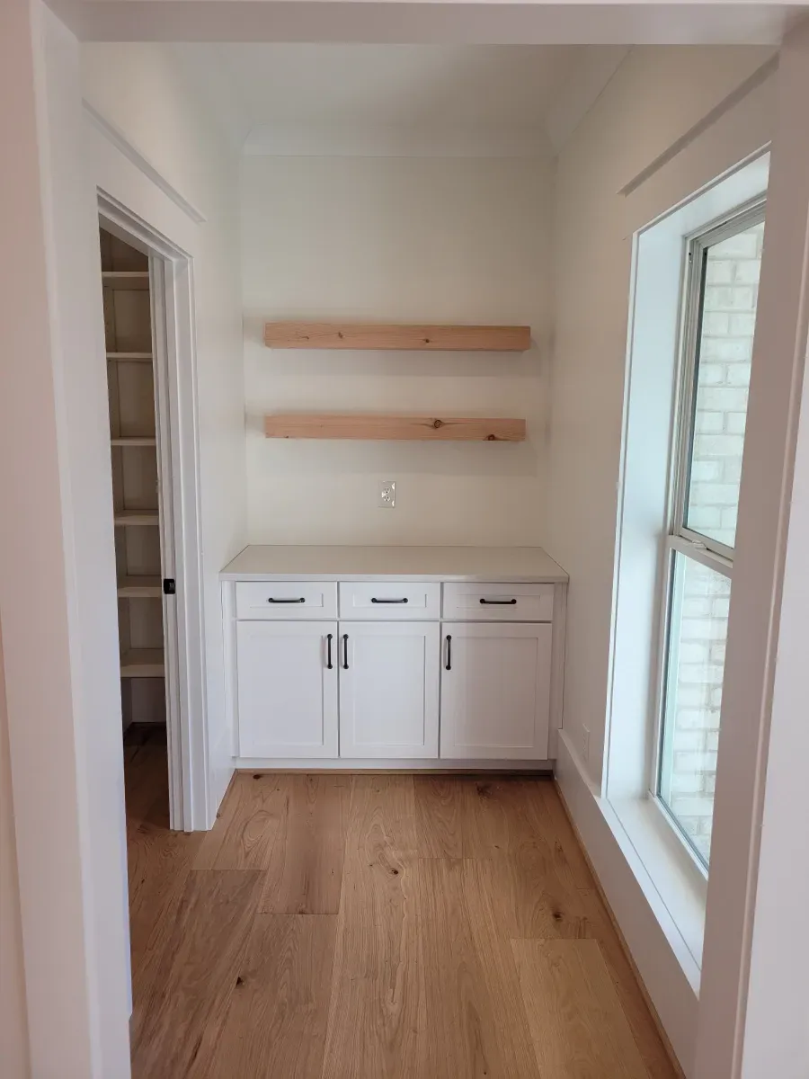 Built-in white cabinets with three doors and two wooden shelves in a room with a window and a door.