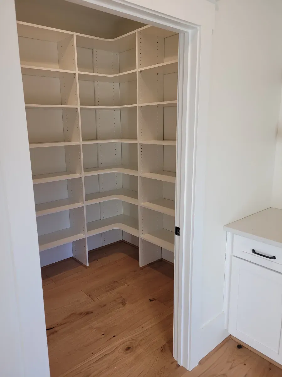 White pantry with built-in shelves on wooden floor, visible through a doorway.