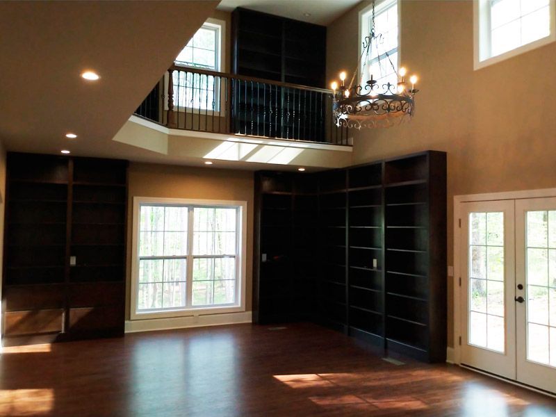A grand, two-story library with built-in bookshelves, a balcony, and a chandelier.