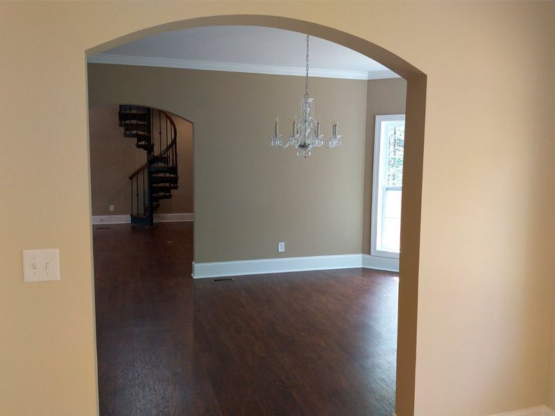 View through an archway into a room with a spiral staircase and chandelier.