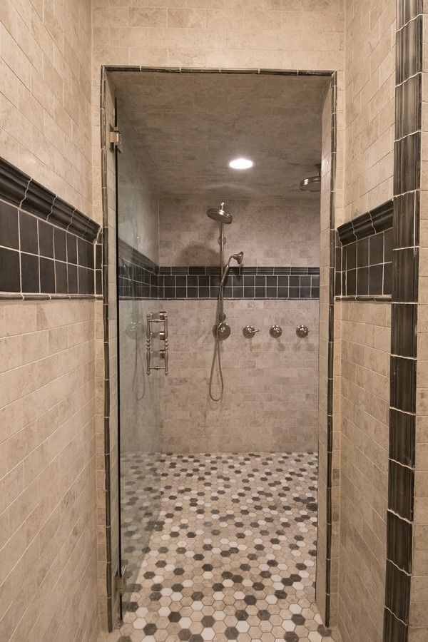 Walk-in shower with glass door, hexagon tile floor, and multiple shower heads. Beige and dark tile accents.
