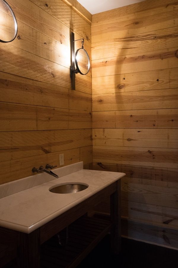 Rustic bathroom with wood-paneled walls, a marble countertop, and a round sink.