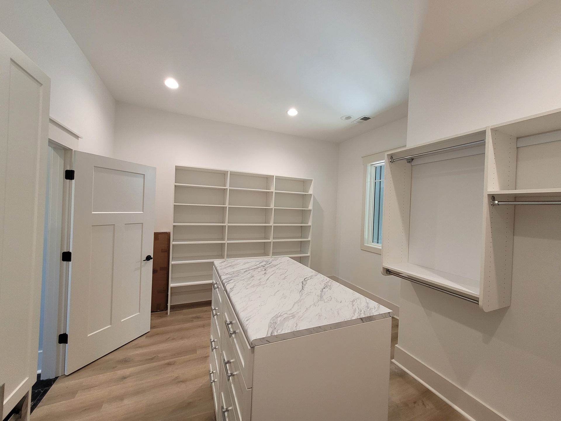 Walk-in closet with white shelving, a central island, and a closed door.