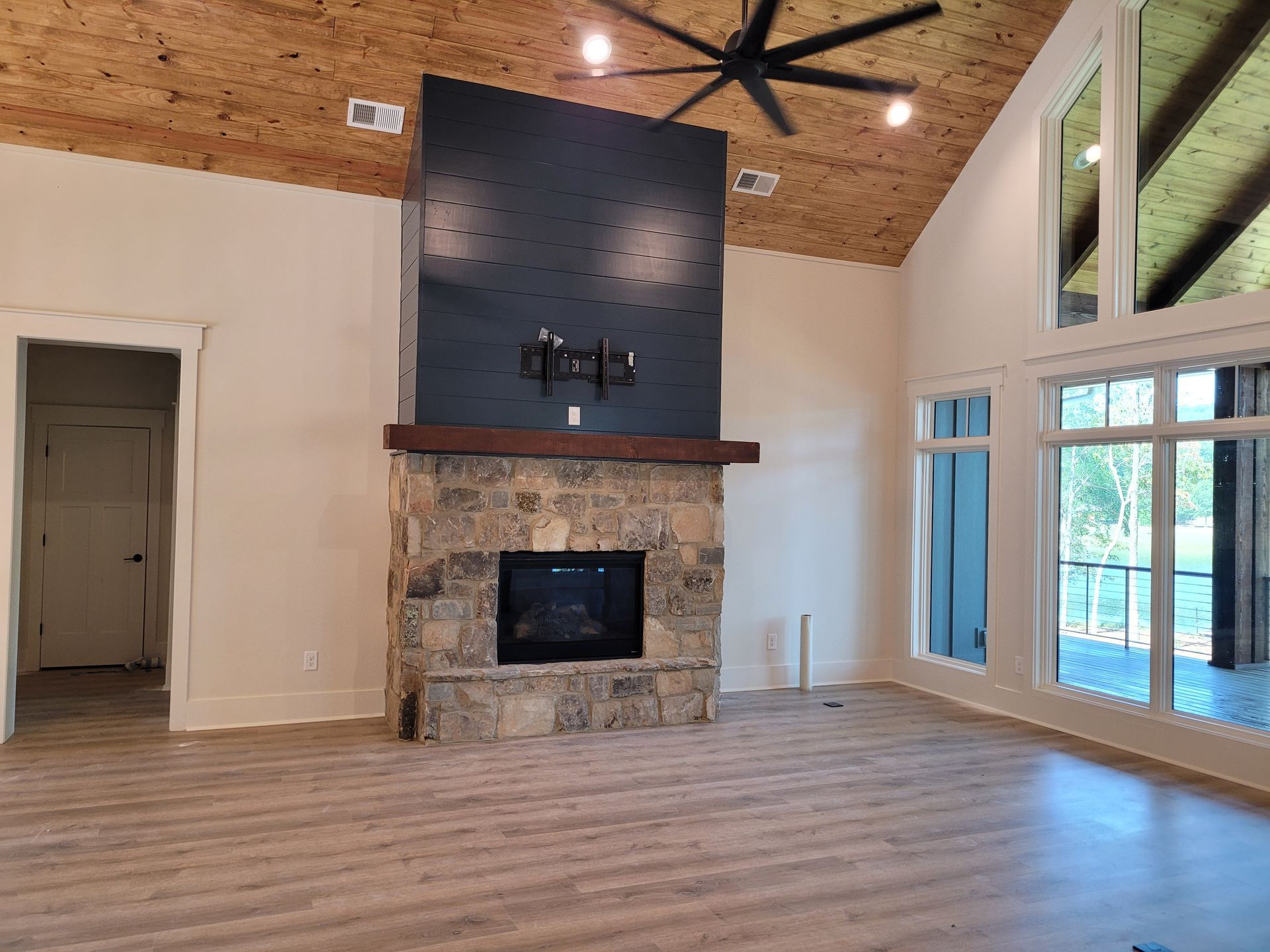Living room with stone fireplace, black accent wall, and large windows.