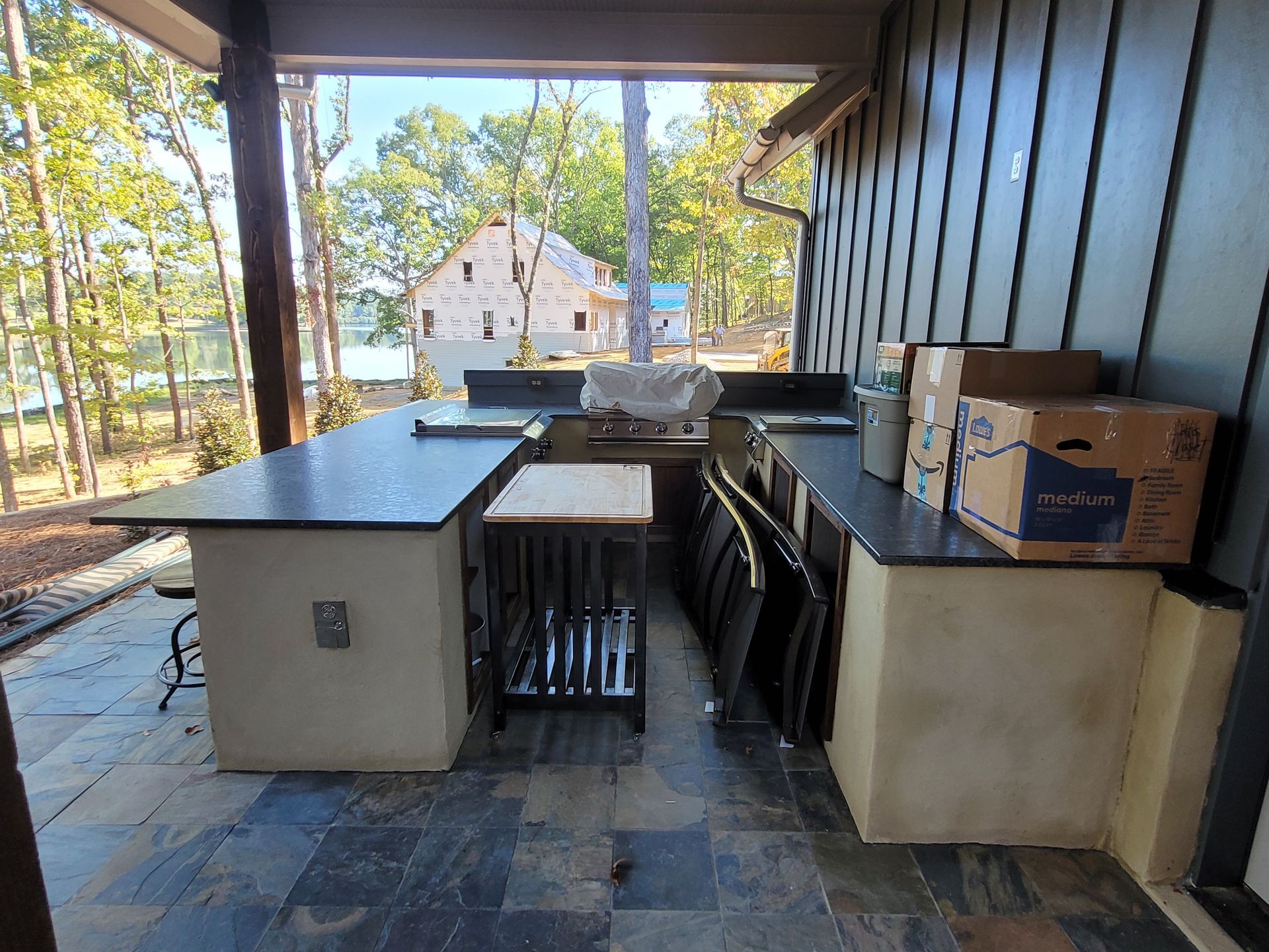Outdoor kitchen with black countertops, grill, and stools under a covered porch.