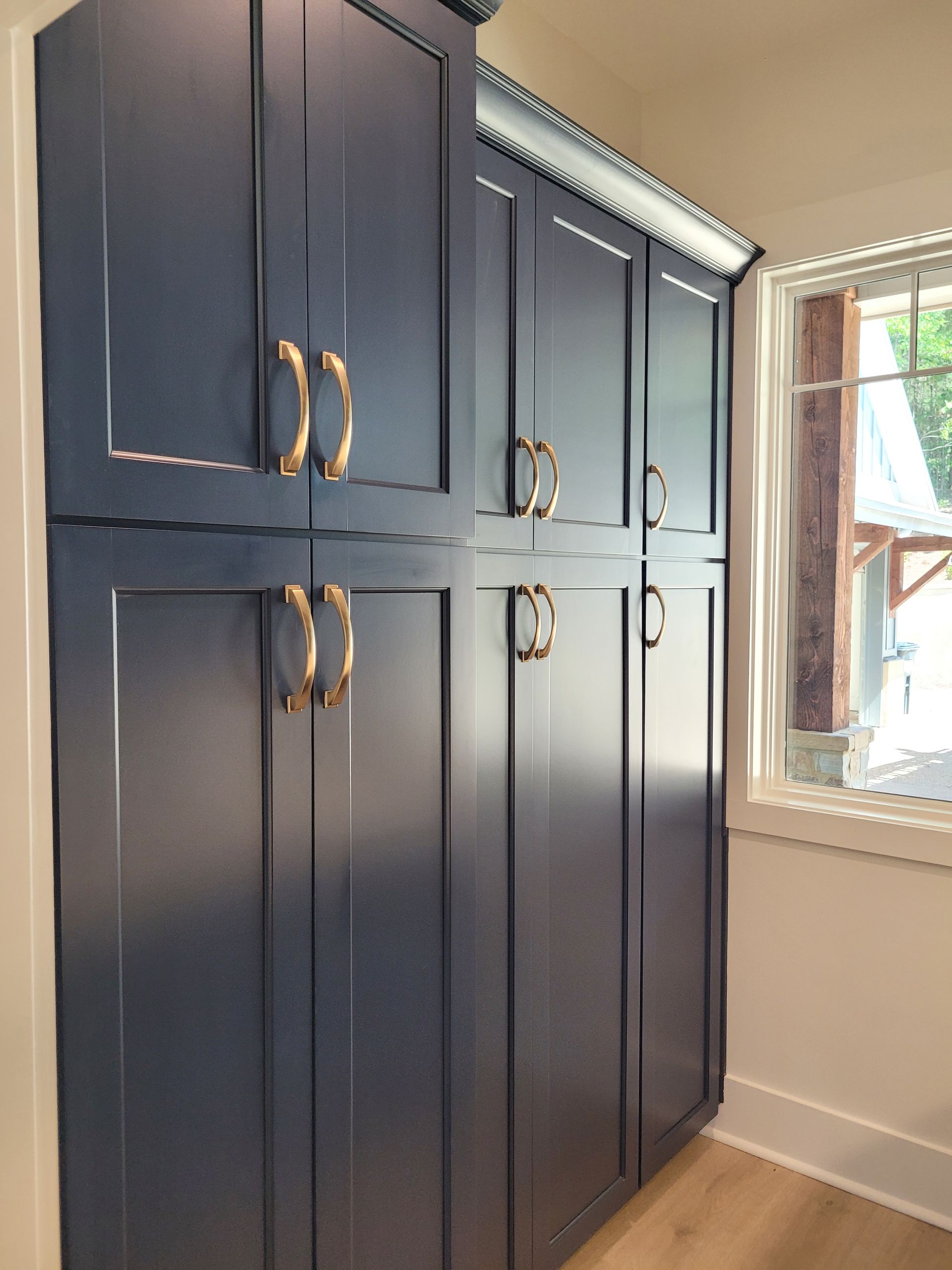 Dark blue cabinets with gold handles near a window with wood trim.