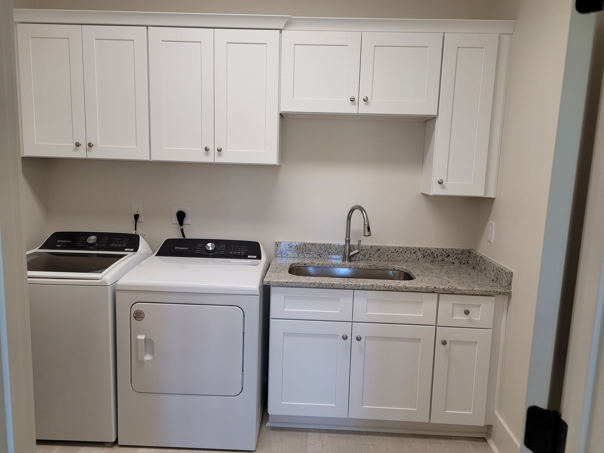 Laundry room with white cabinets, washer, dryer, sink, and granite countertop.