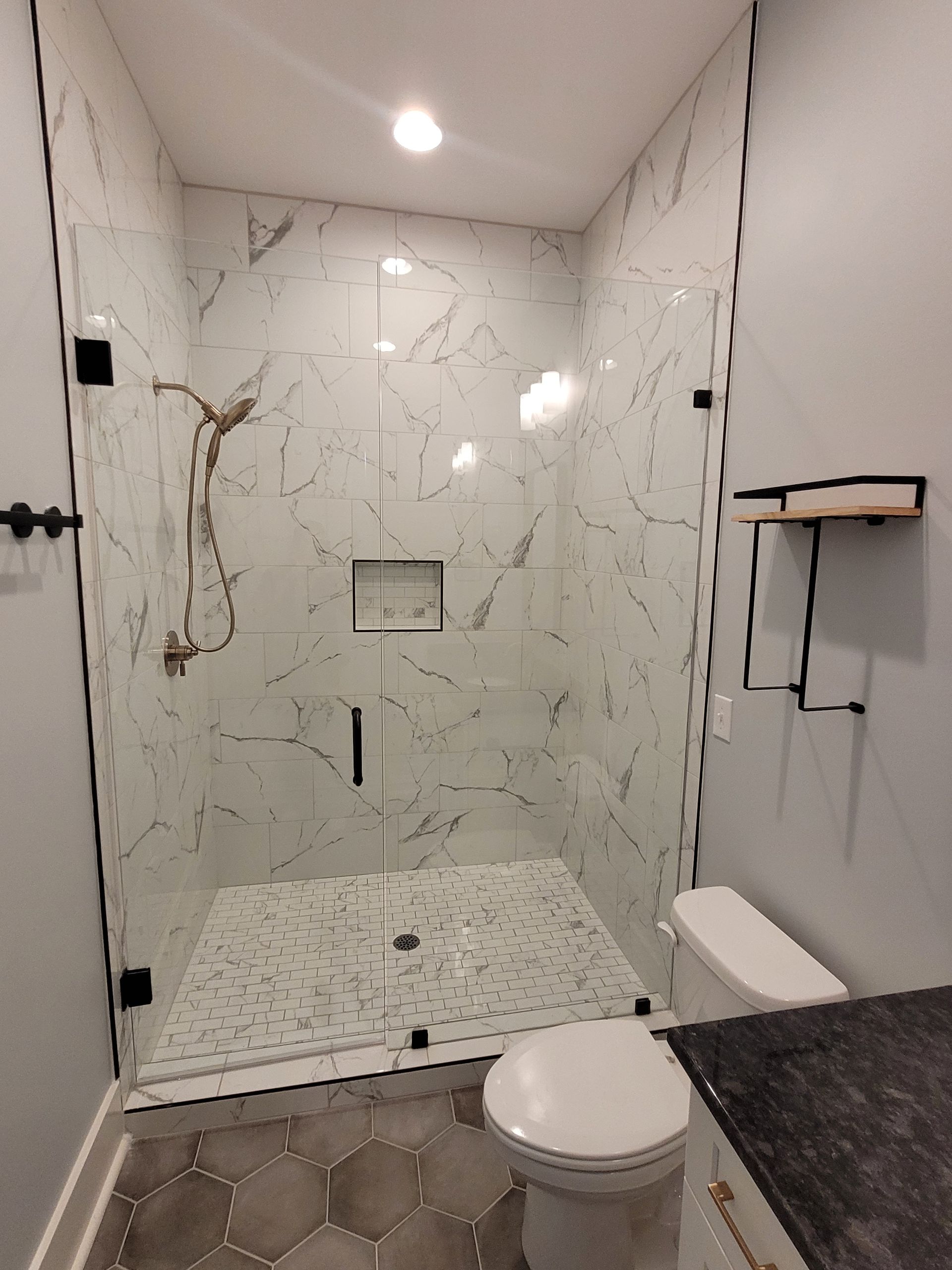 Modern shower with white marble tile, glass doors, and black fixtures in a bathroom.