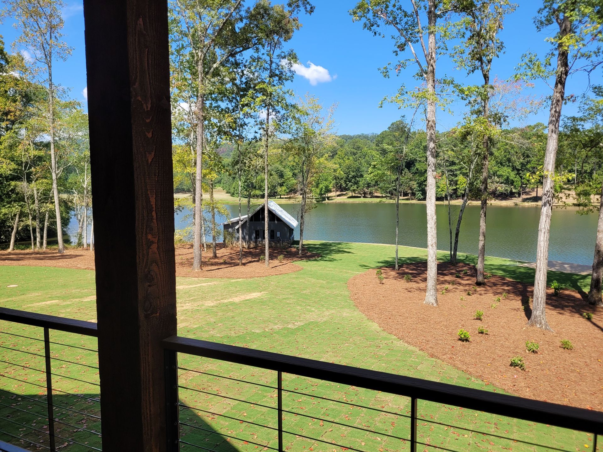 Lakeside view from a porch with a grassy yard, trees, and a dock on a sunny day.