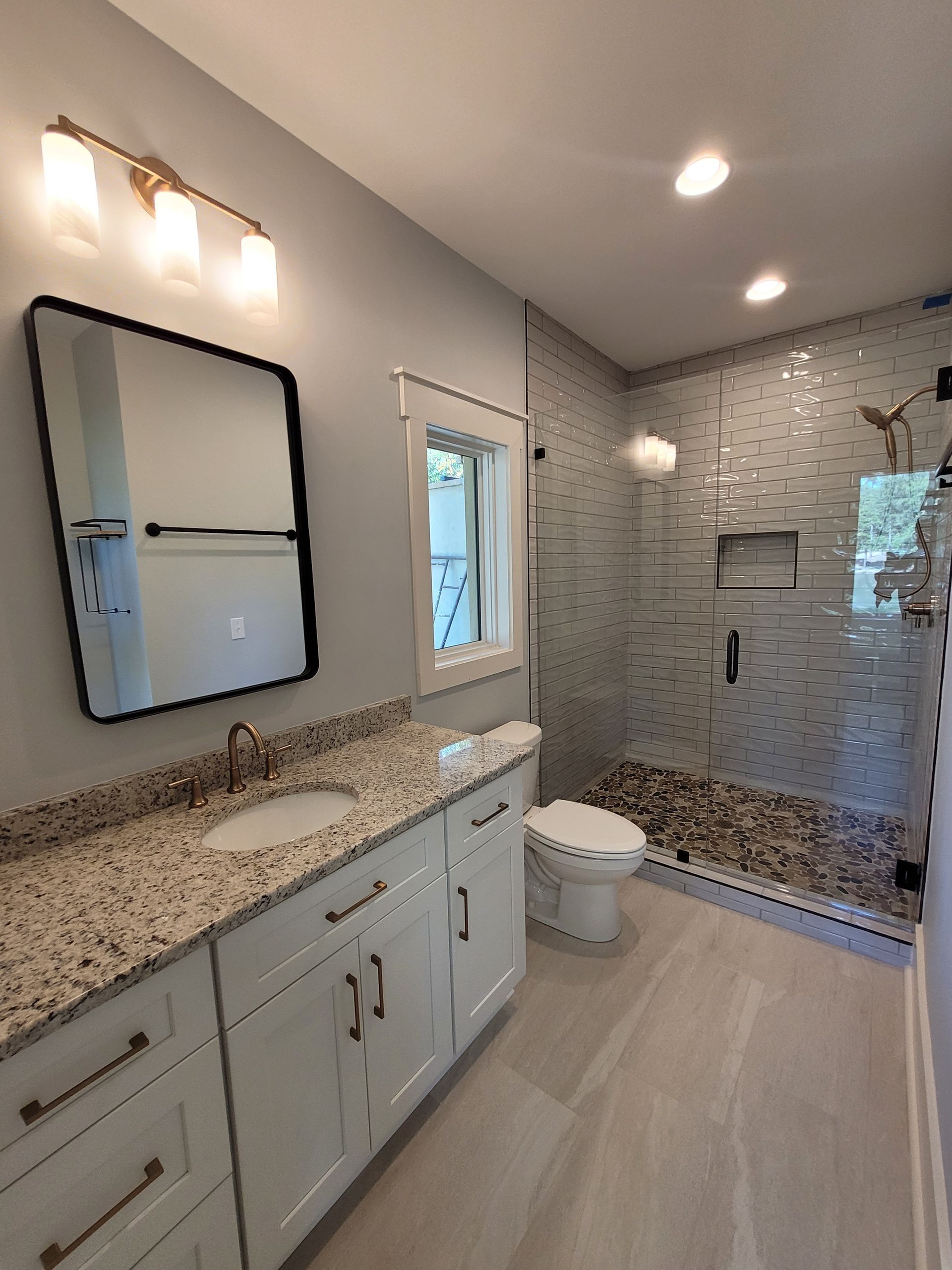 Bathroom with white cabinets, granite countertop, glass shower, and pebble floor.