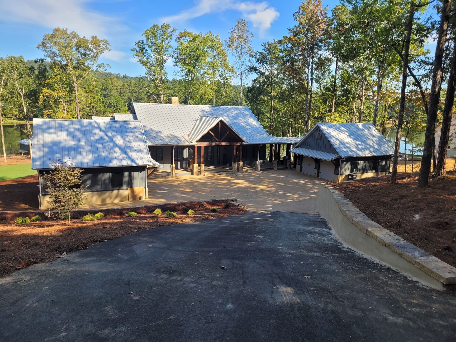 House with a light gray roof, surrounded by trees. Driveway leads to the house.