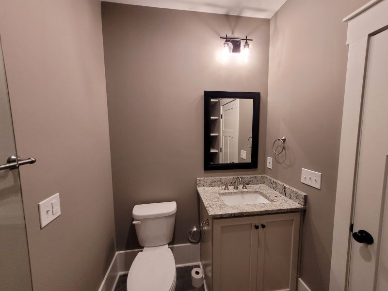 Small bathroom with toilet, vanity, mirror, and dark gray walls.