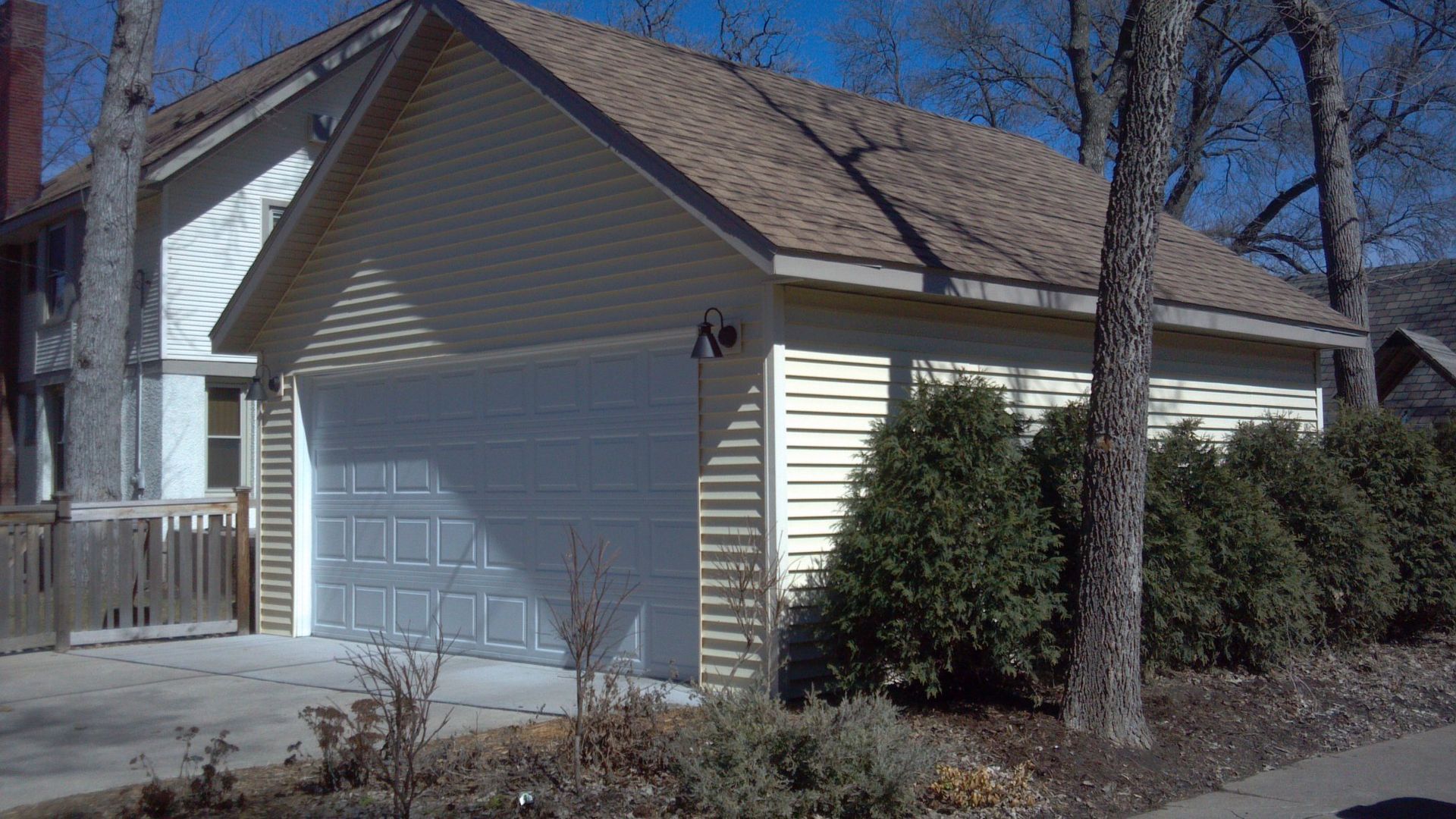 A white garage with a brown roof is next to a house