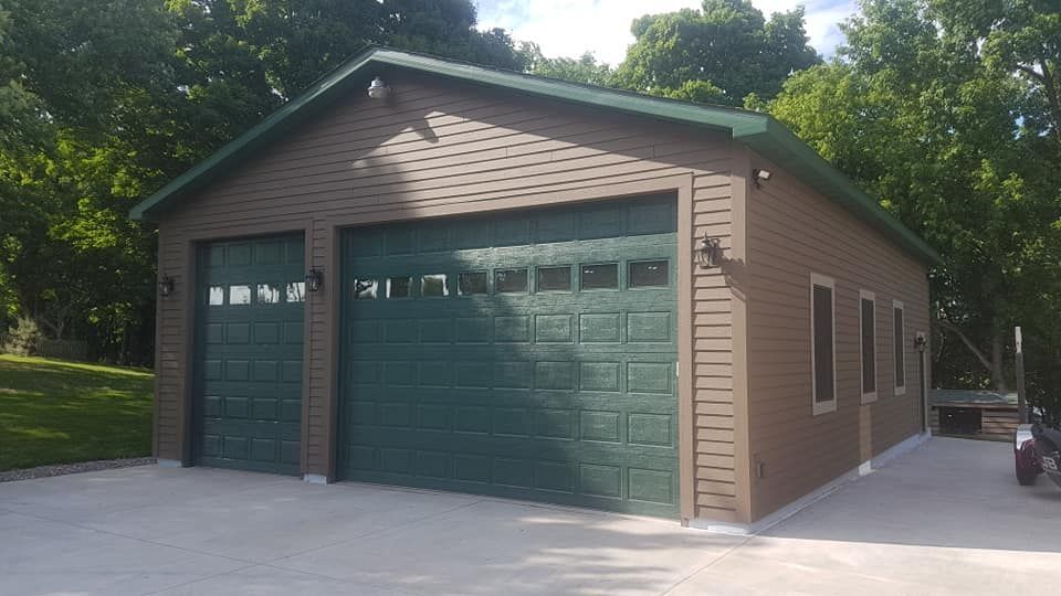 A garage with two green garage doors and a green roof.