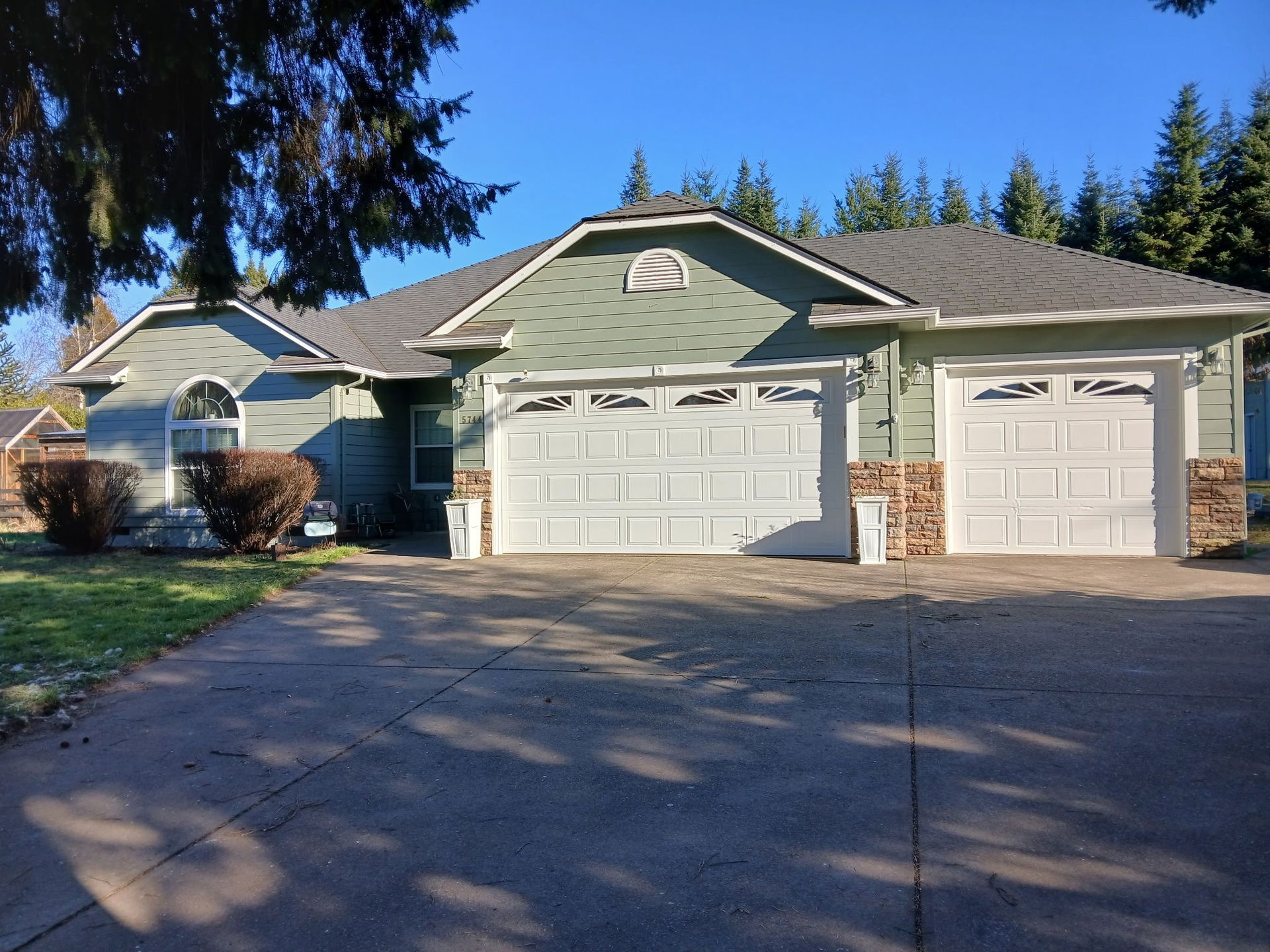 Suburban house with two garages, green siding, and a driveway under bright blue sky.