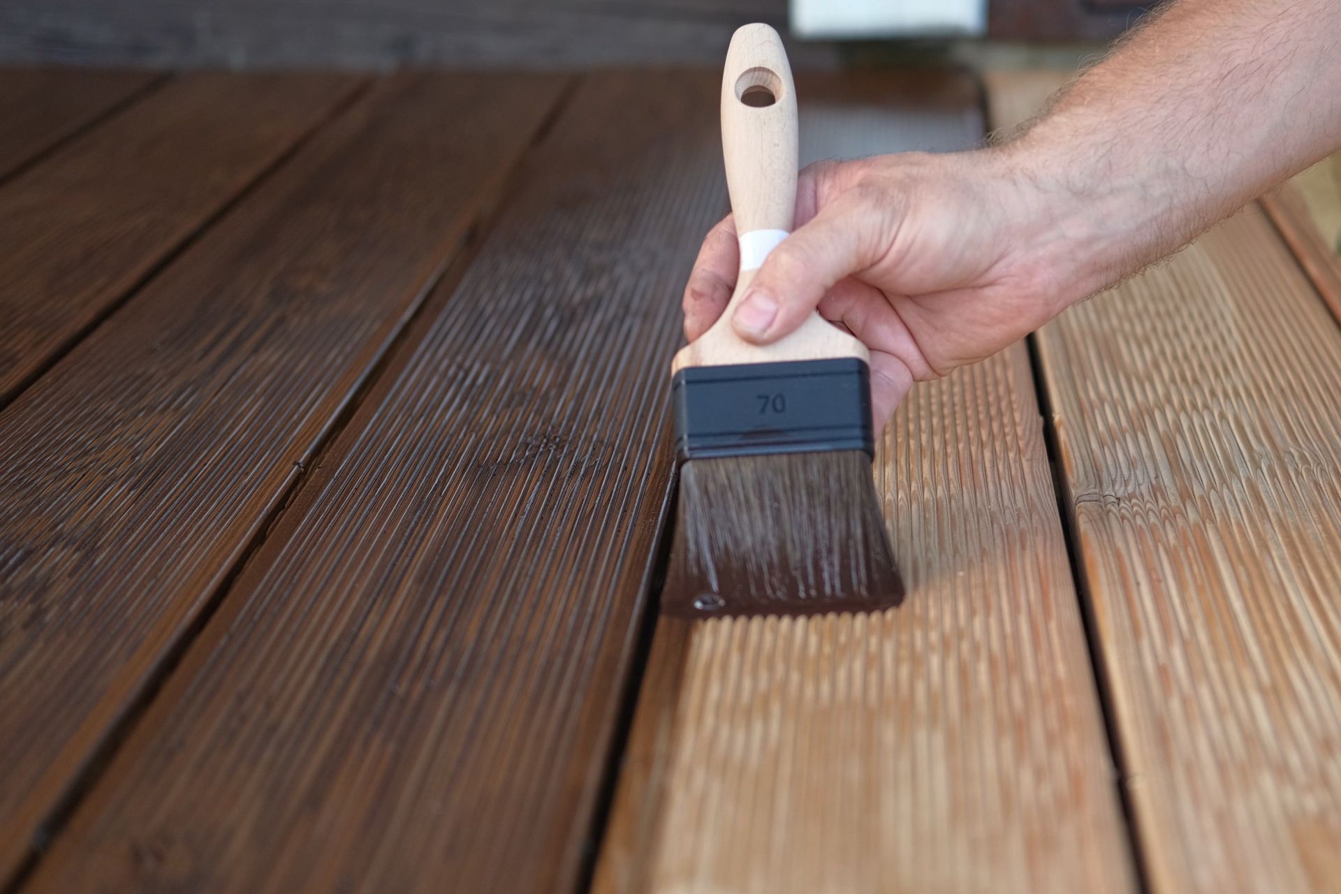 Hand brushing brown wooden deck boards with stain