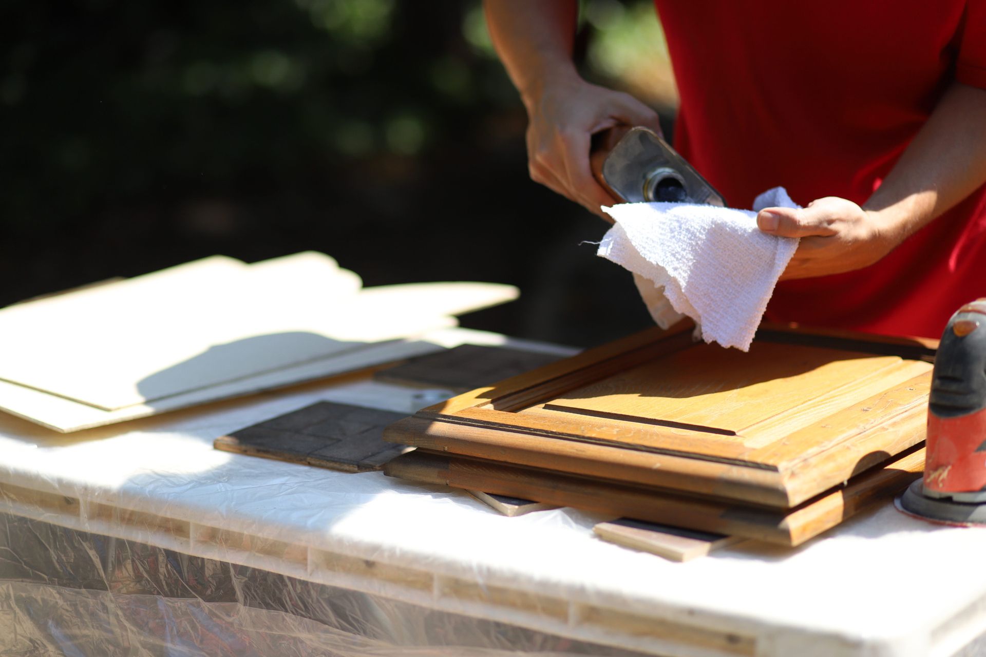 Hands holding a spray bottle and cloth, cleaning stacked wooden panels on a table.