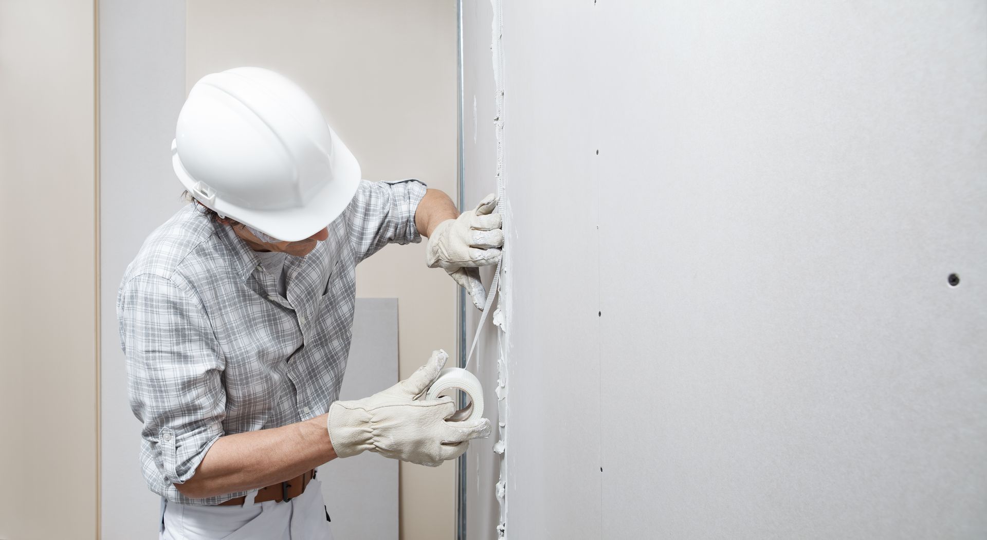 Construction worker in white hard hat installing wiring inside a wall Construction worker in white hard hat installing wiring inside a wall