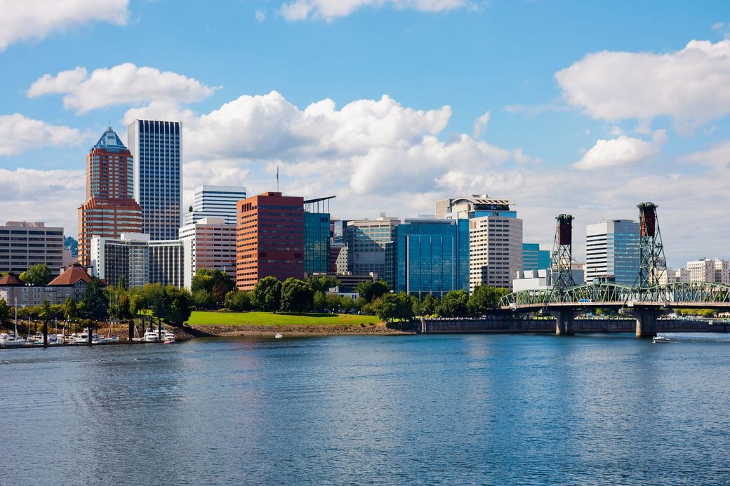 Waterfront city skyline with tall buildings, bridge, and calm blue water under a clear sky