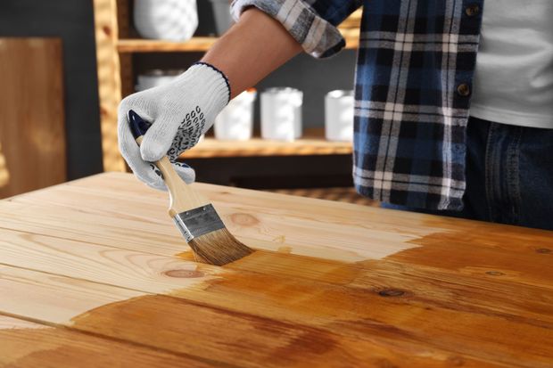 Gloved hand applying varnish to a wooden tabletop with a brush
