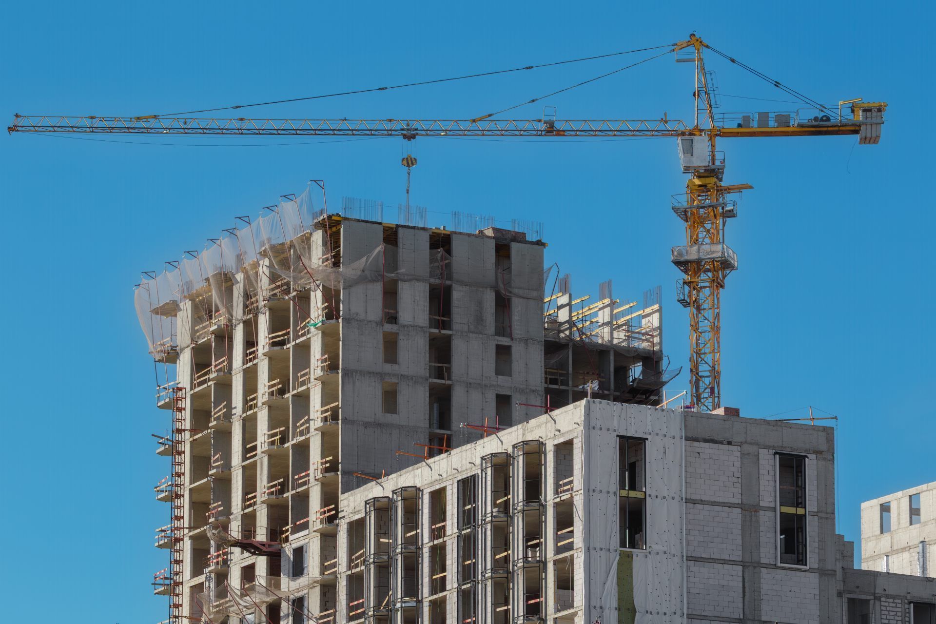 Construction site: crane over a multi-story concrete building under construction, blue sky.