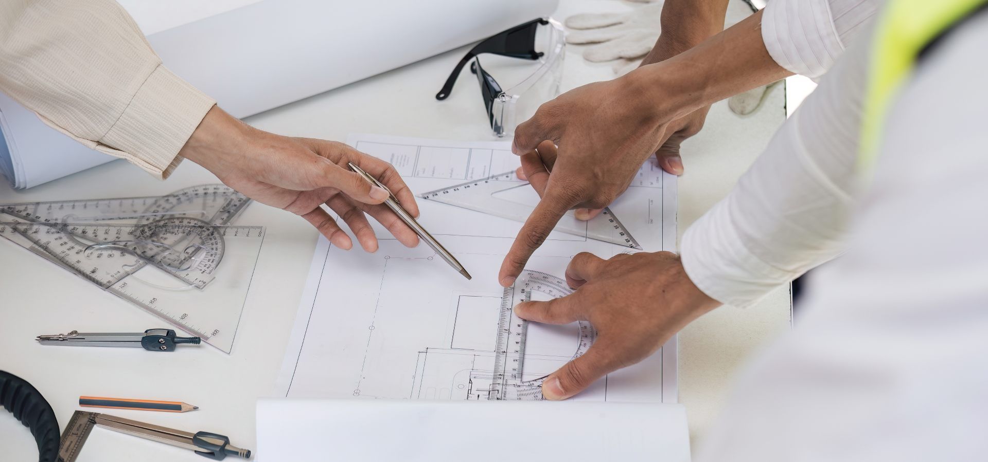 People pointing and discussing blueprints on a table with drafting tools.