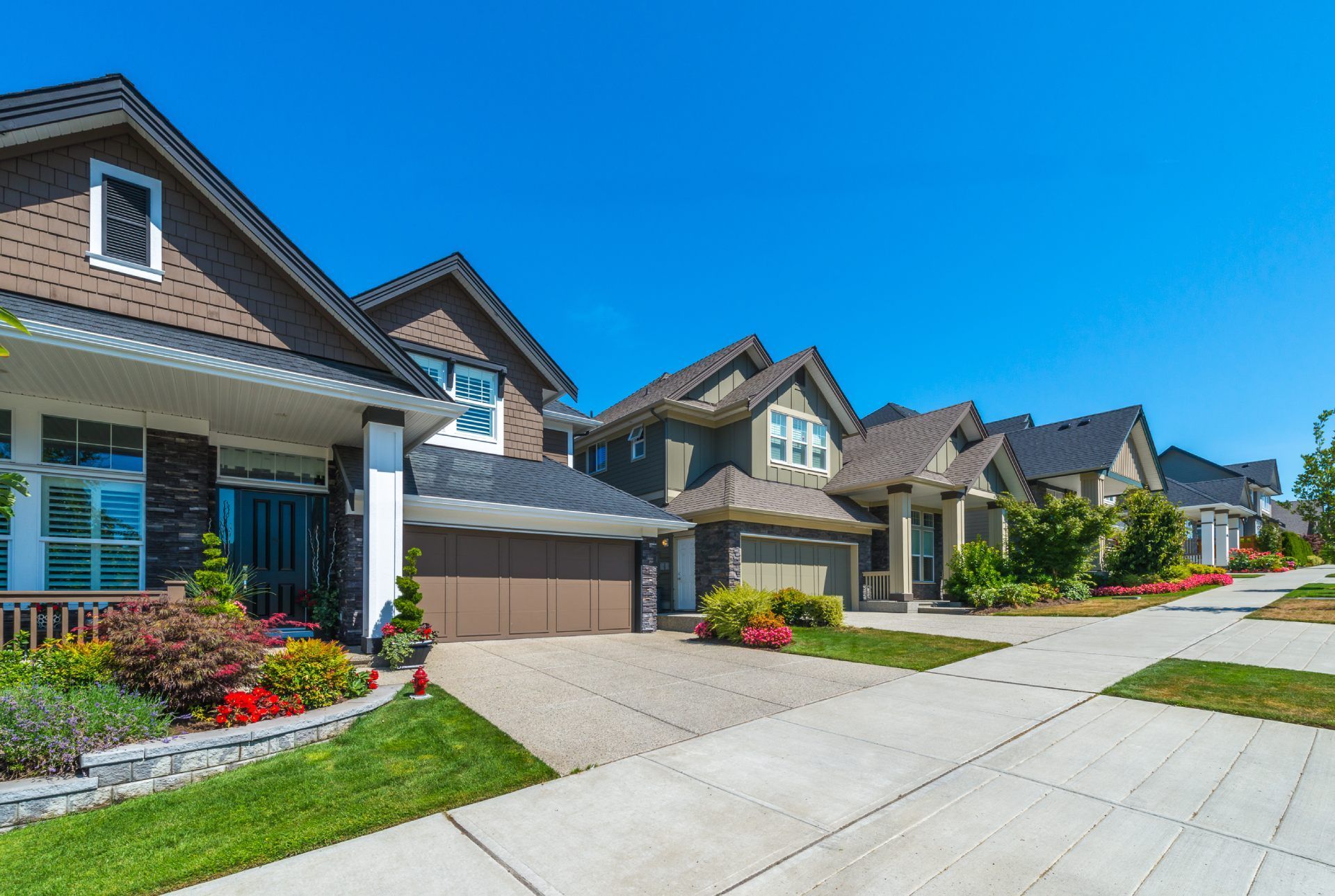 Row of houses with brown roofs, beige garages, and green lawns under a blue sky.