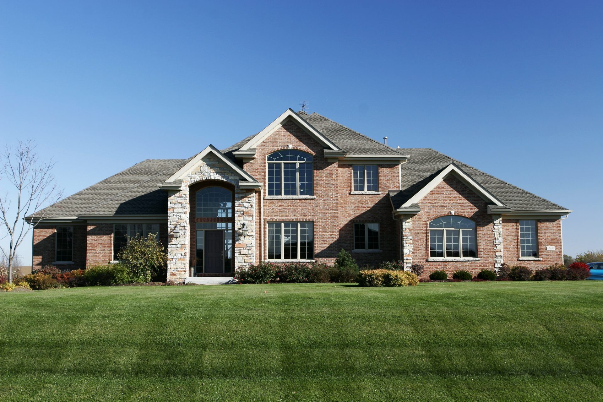 Brick two-story house with green lawn against blue sky.