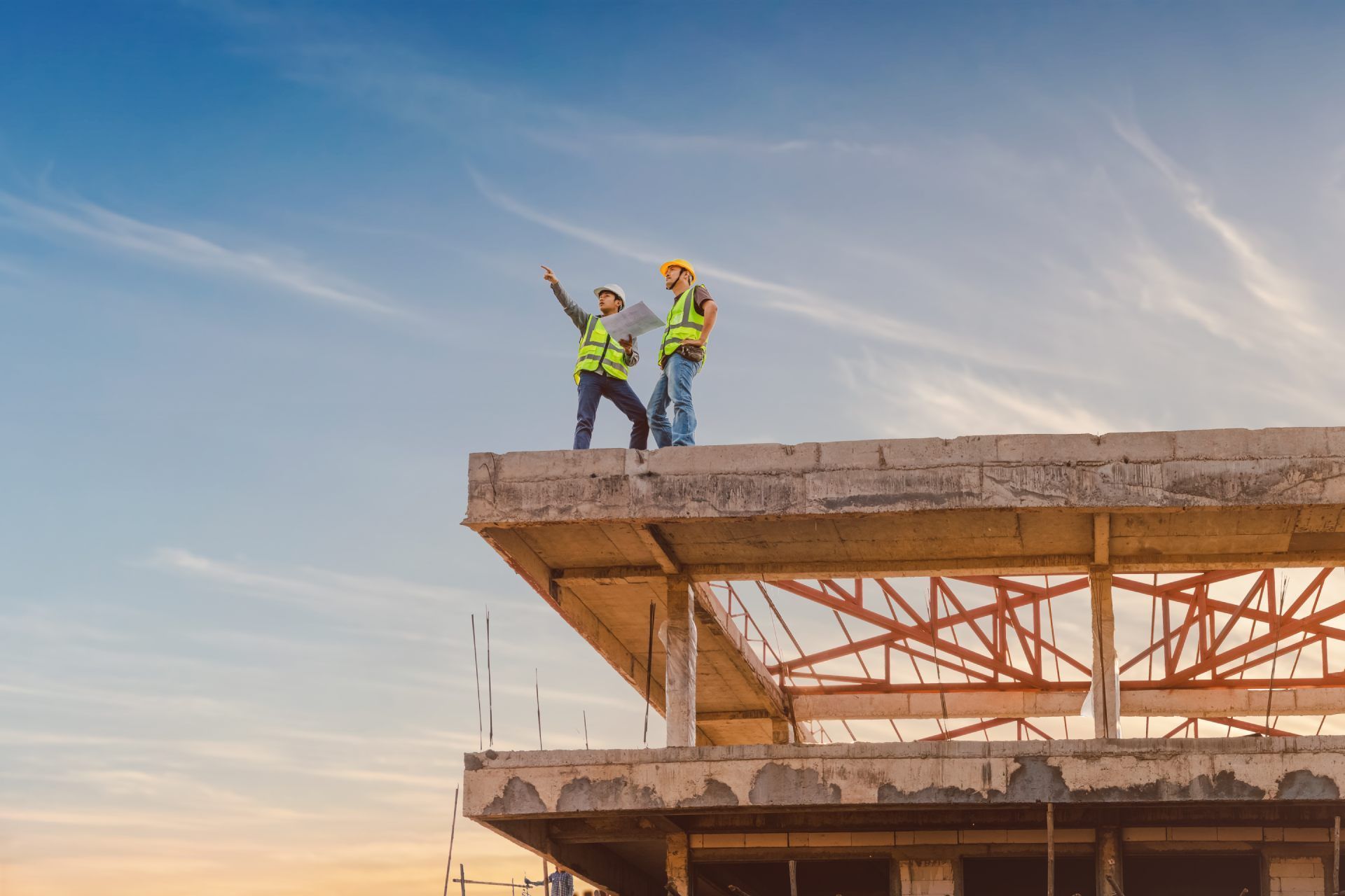 Construction workers on a building rooftop, pointing at the horizon under a blue sky.