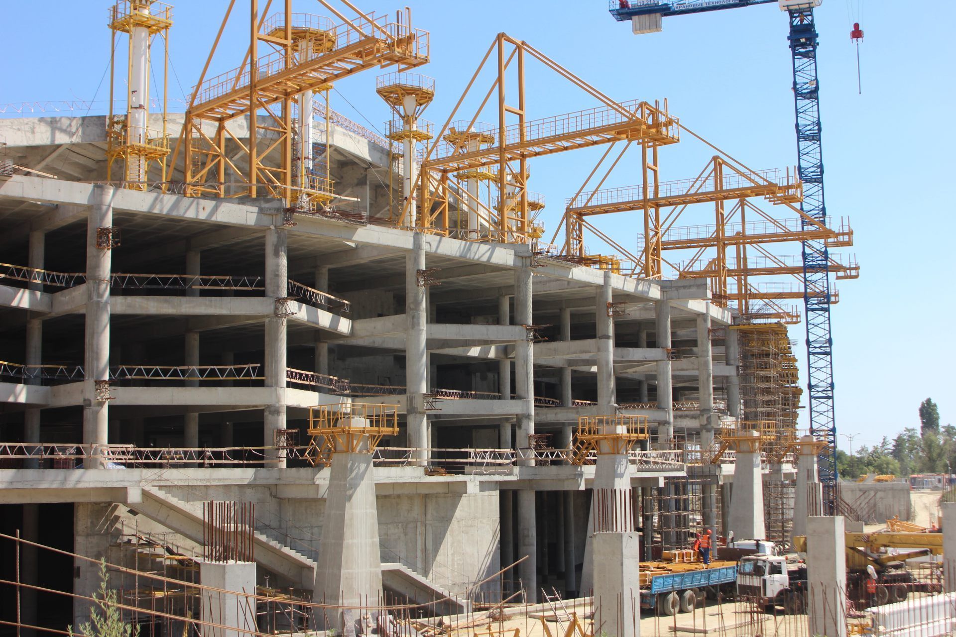 Construction site with multiple yellow tower cranes and a large concrete building frame under construction.